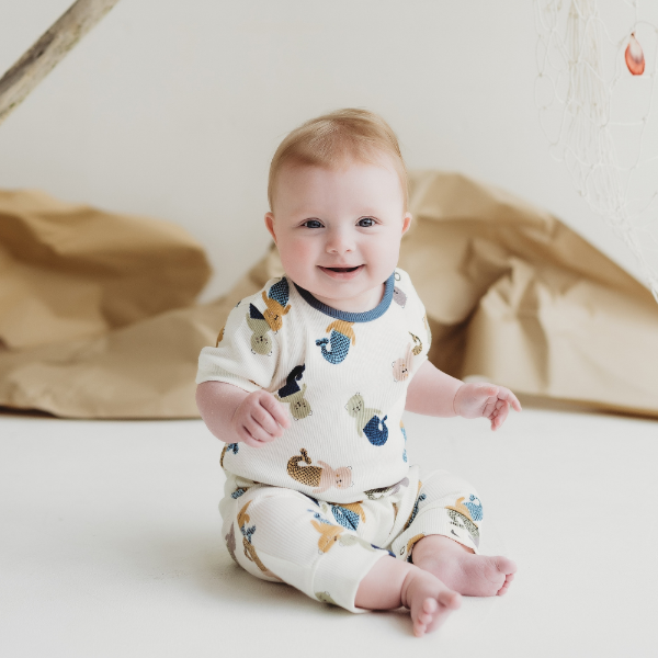 Baby wearing a sleepsuit with animal prints sitting on a white surface.