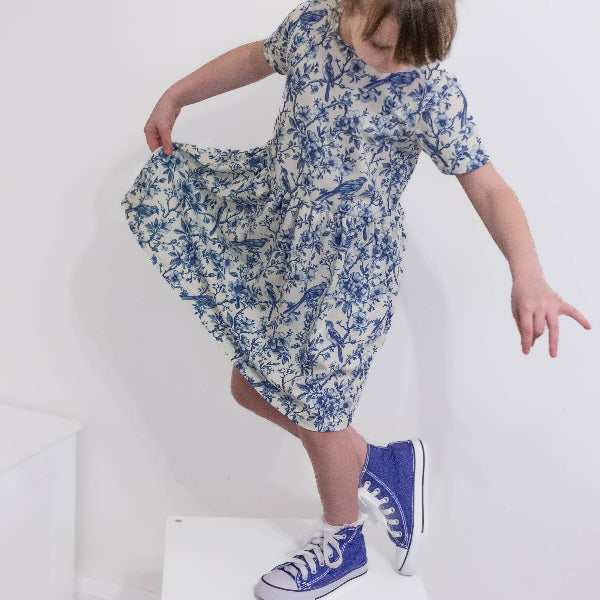 Child wearing a blue floral dress and blue high-top sneakers on a white background
