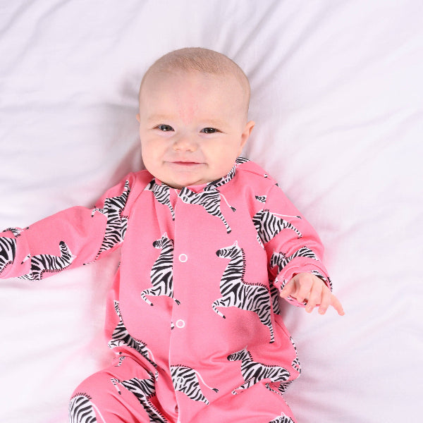 Baby wearing a pink onesie with zebra patterns on a white background