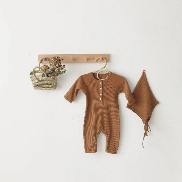 Brown baby romper and hat hanging on a wooden hook against a white wall.