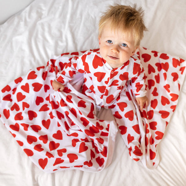 Baby wrapped in a red heart-patterned blanket on a white surface