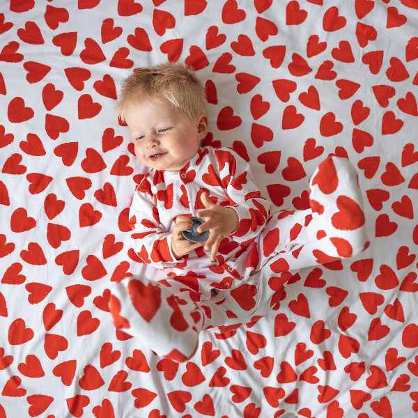 Baby lying on a white blanket with red heart pattern