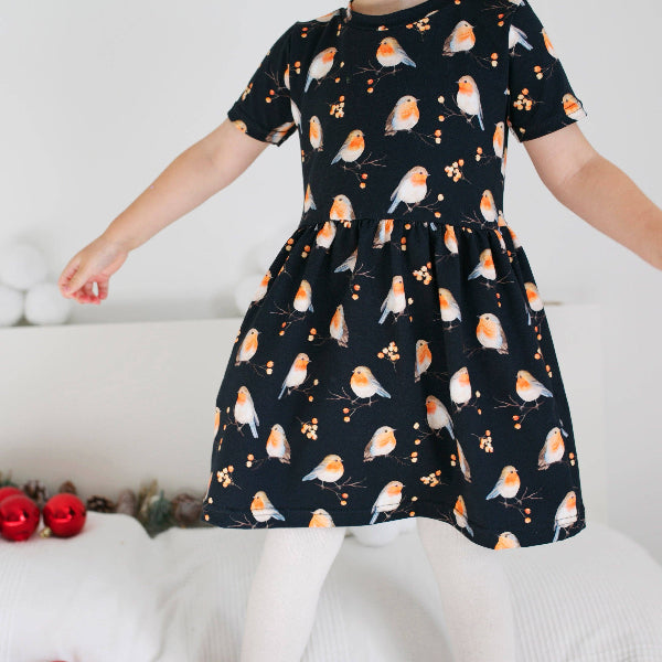 Child wearing a black dress with bird pattern on a white background