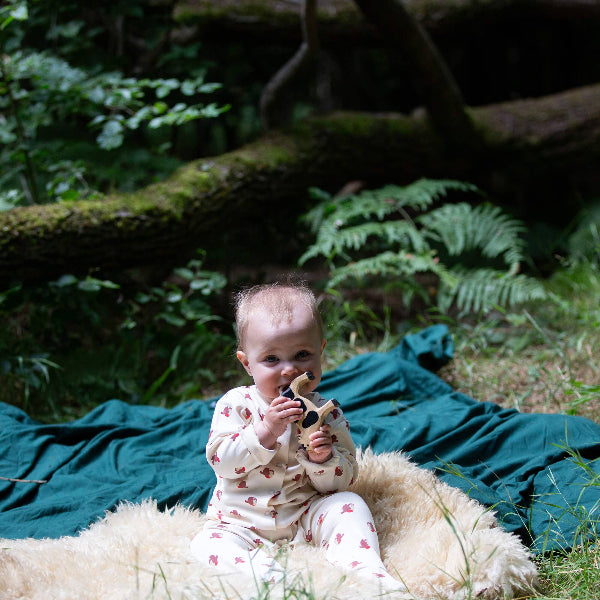 Baby sitting on a fluffy rug in a forest setting with a blue blanket and greenery.