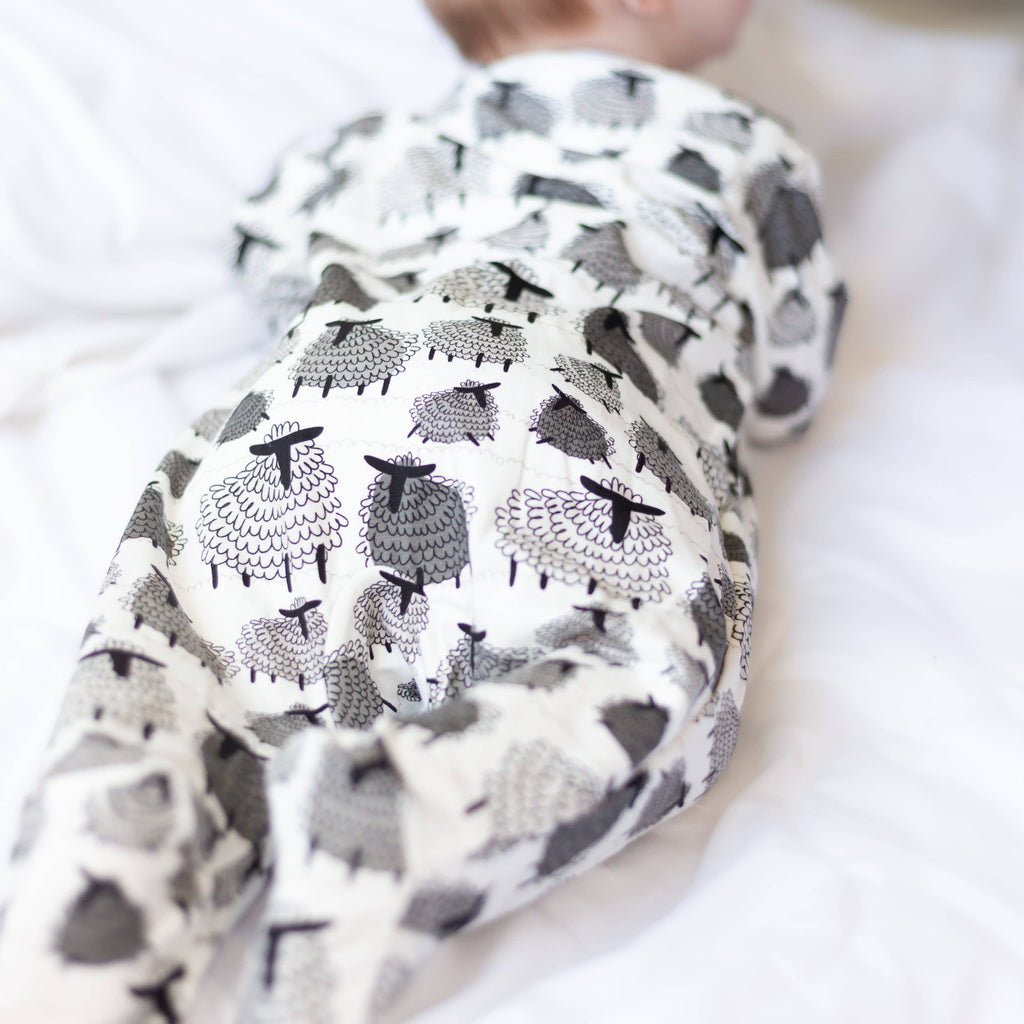 Baby wearing a sleepsuit with black and white sheep pattern on a white background