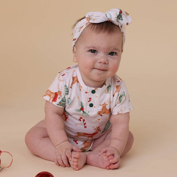 Baby wearing a onesie with animal prints and a matching headband on a beige background