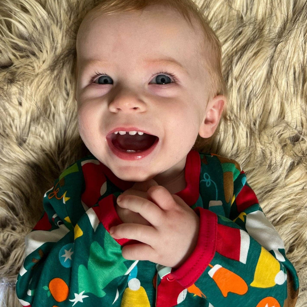 Child wearing a colorful outfit with a pattern of stars, snowmen, and candy canes on a fluffy beige rug.