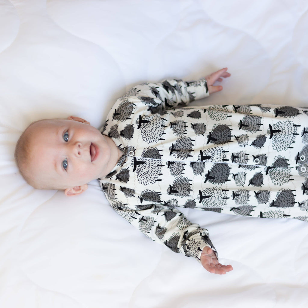 Baby wearing a sleepsuit with sheep pattern on a white blanket