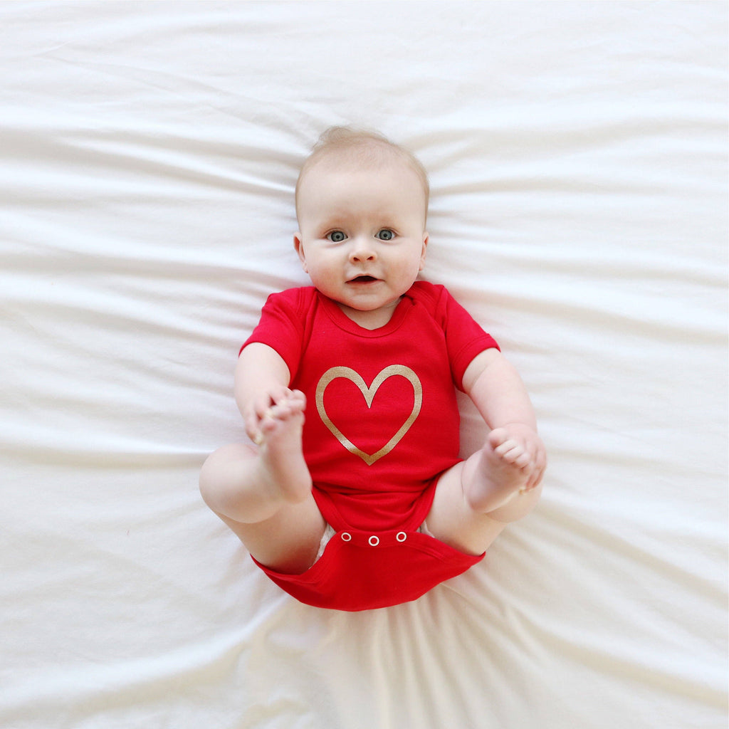 Baby wearing a red vest with a gold heart on a white background