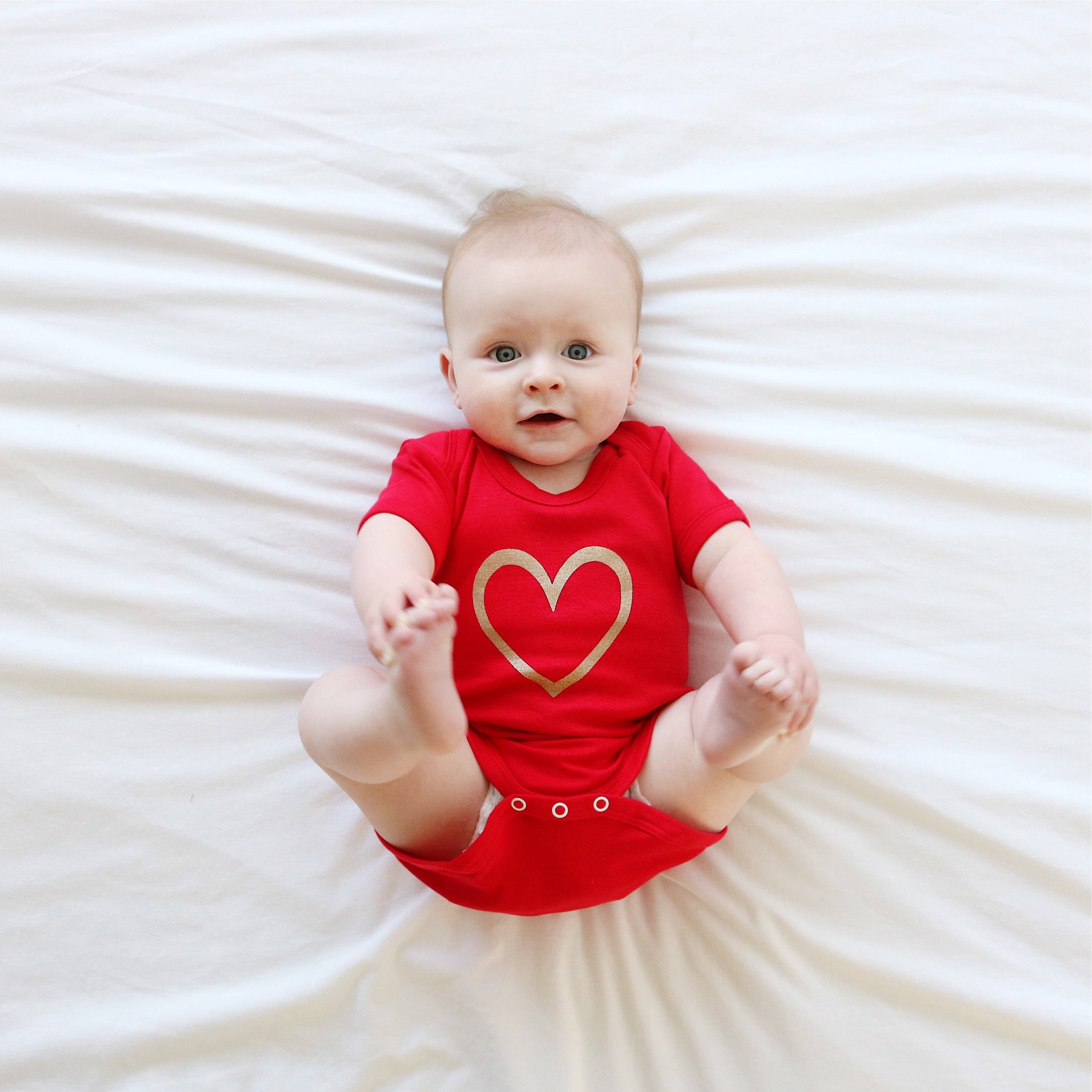 Baby wearing a red vest with a gold heart on a white background