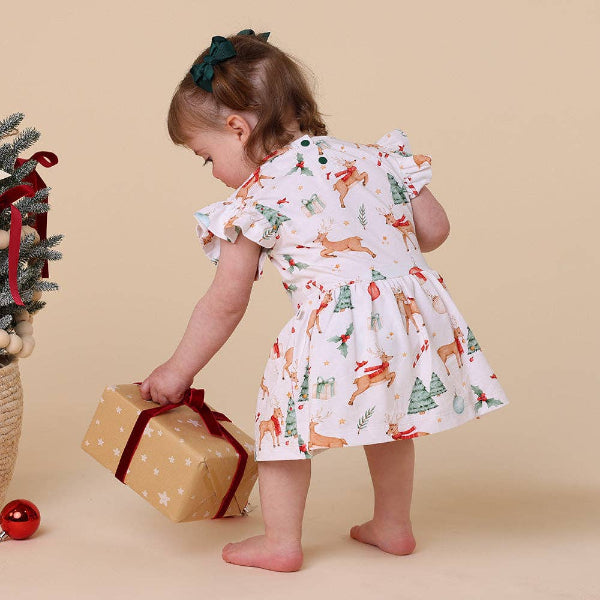 Child in a festive dress holding a gift box with a Christmas tree and presents on a beige background