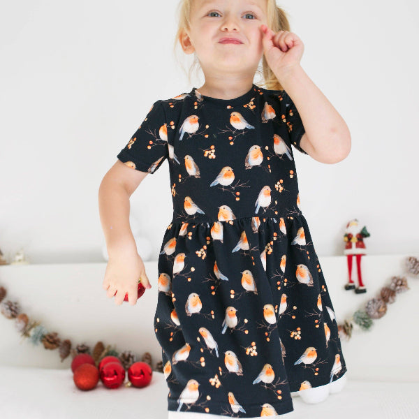 Child wearing a black dress with bird pattern against a white background