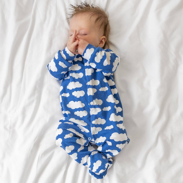 Baby wearing a blue onesie with white cloud pattern on a white background