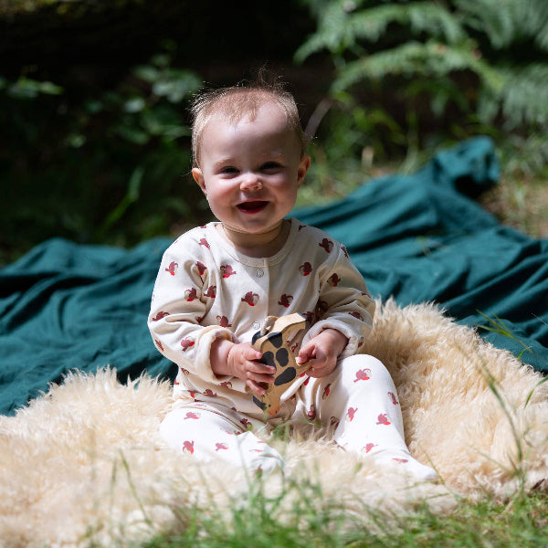 Baby sitting on a fluffy surface outdoors holding a wooden toy