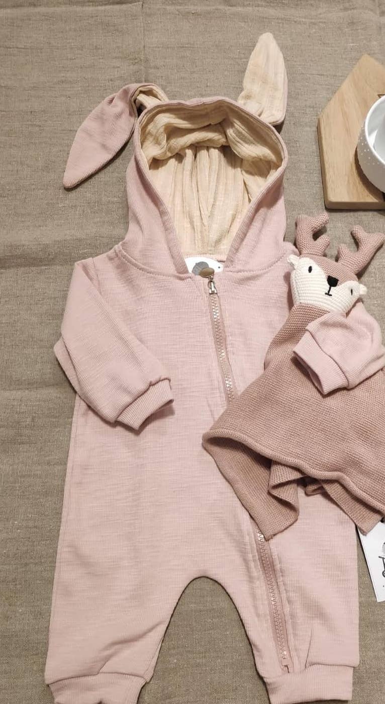 Pink baby sleepsuit with bunny ears on a textured surface