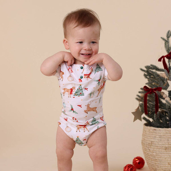 Baby wearing a Christmas-themed onesie with a beige background and a small Christmas tree.
