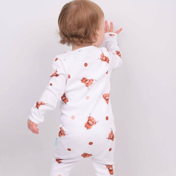 Baby wearing a white sleepsuit with orange floral patterns on a plain background