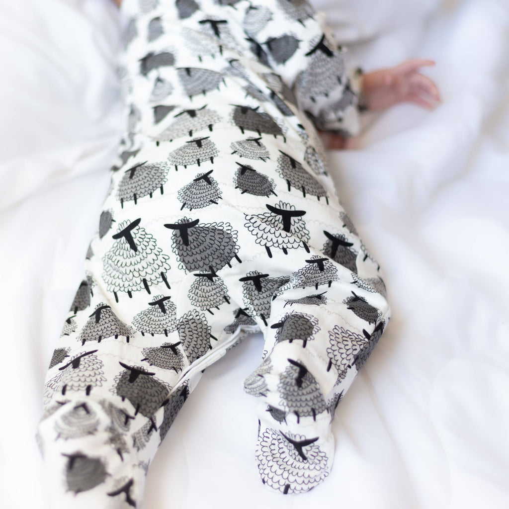Baby wearing a sleepsuit with black and white sheep pattern on a white background