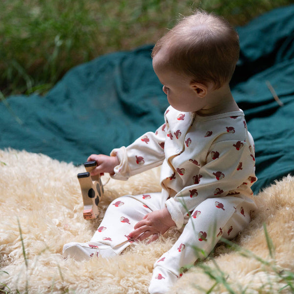 Baby in white pajamas with red patterns sitting on a fluffy surface outdoors.