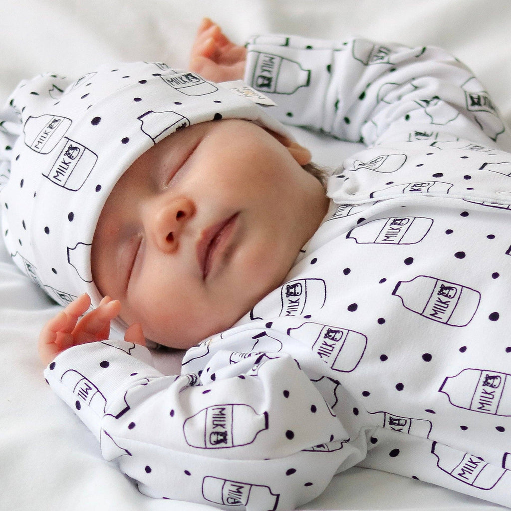 Baby wrapped in a white sleepsuit with black milk bottle patterns