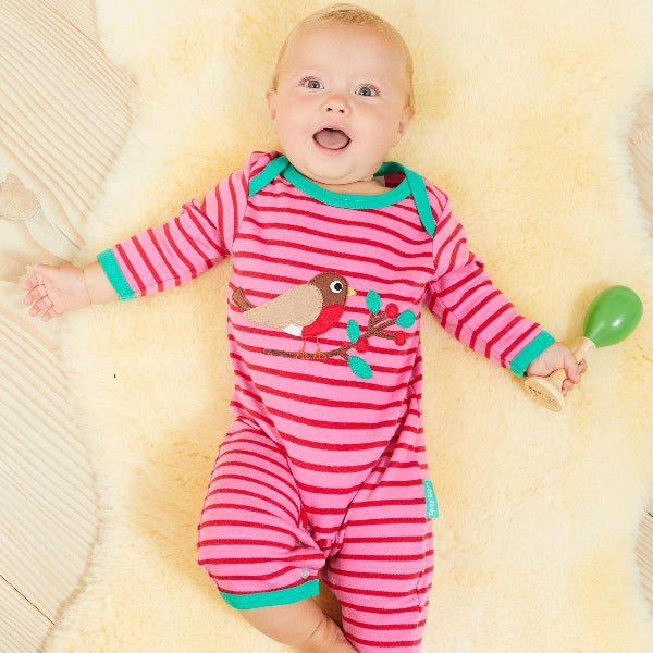 Baby in a pink and green striped outfit lying on a yellow blanket