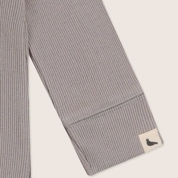 Gray ribbed bodysuit sleeve with a brand label on a light beige background