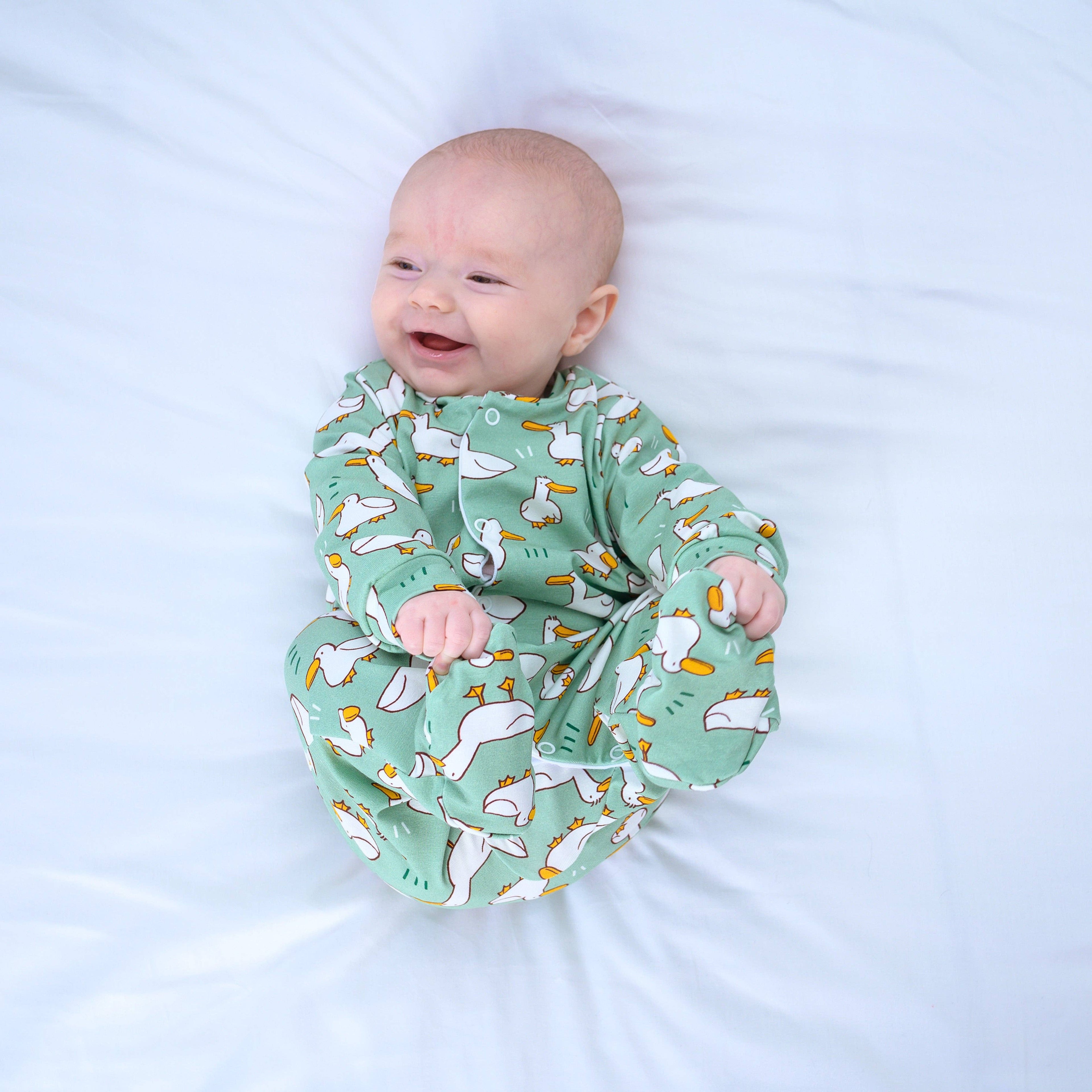 Baby wearing a green sleepsuit with animal patterns on a white background