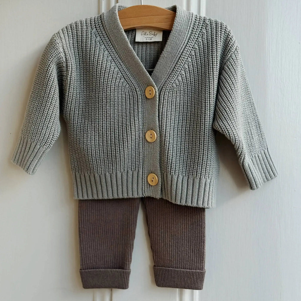 Baby sweater and pants set on a hanger against a white wall