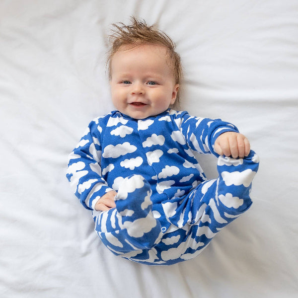 Baby wearing a blue onesie with white cloud patterns on a white background