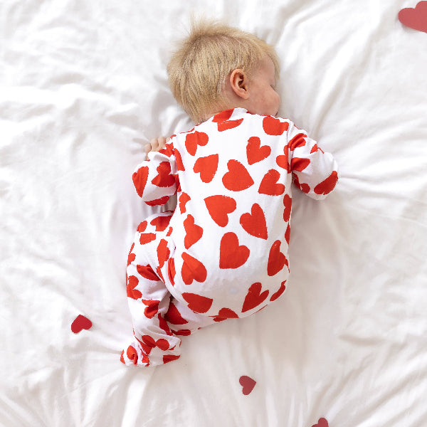 Child wearing a red heart patterned onesie lying on a white surface.