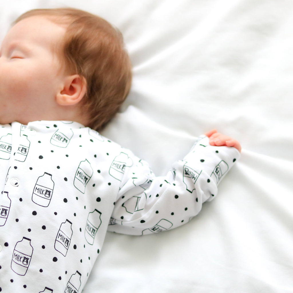 Baby wearing a white sleepsuit with black milk bottle patterns on a white background
