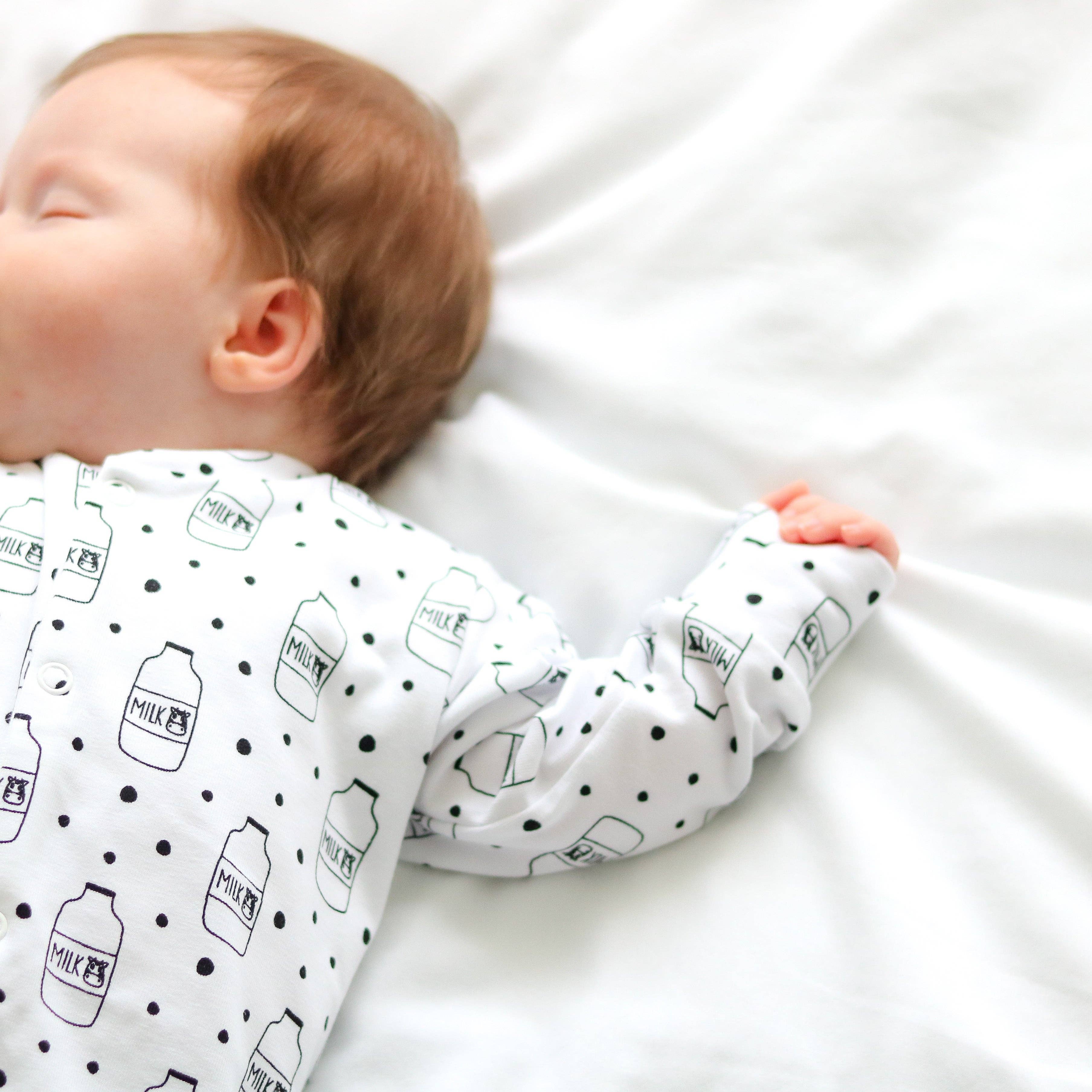 Baby wearing a white sleepsuit with black milk bottle patterns on a white background