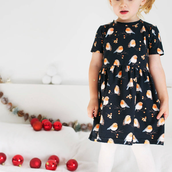 Child wearing a dress with bird pattern in front of Christmas decorations