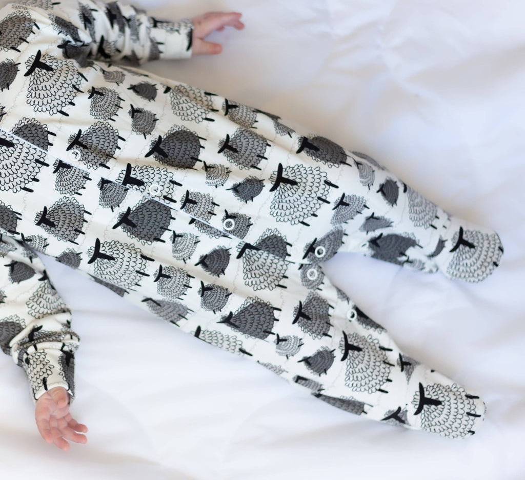 Baby wearing a black and white patterned sleepsuit on a white blanket