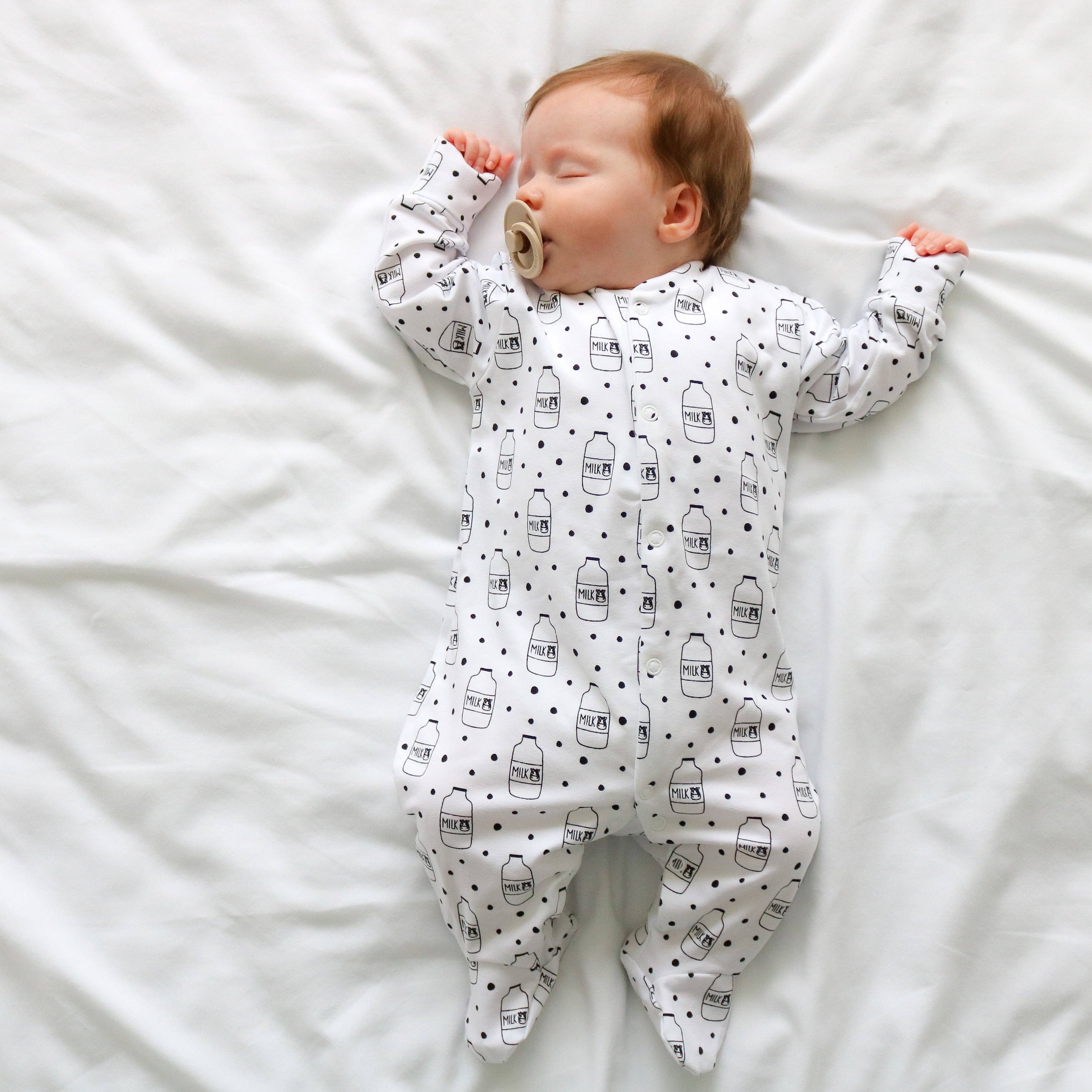 Baby lying on a white bed wearing a sleepsuit with bottle patterns