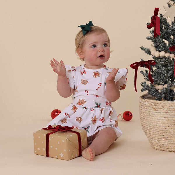 Baby in a festive outfit with a Christmas tree and presents on a beige background