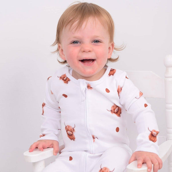 Baby wearing a white sleepsuit with brown animal prints, sitting on a white chair.