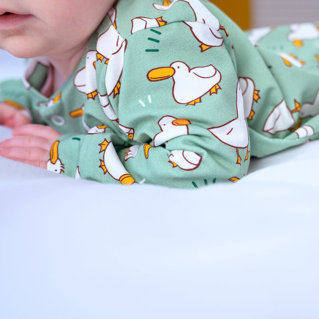 Green sleepsuit with duck pattern worn by a child on a white background