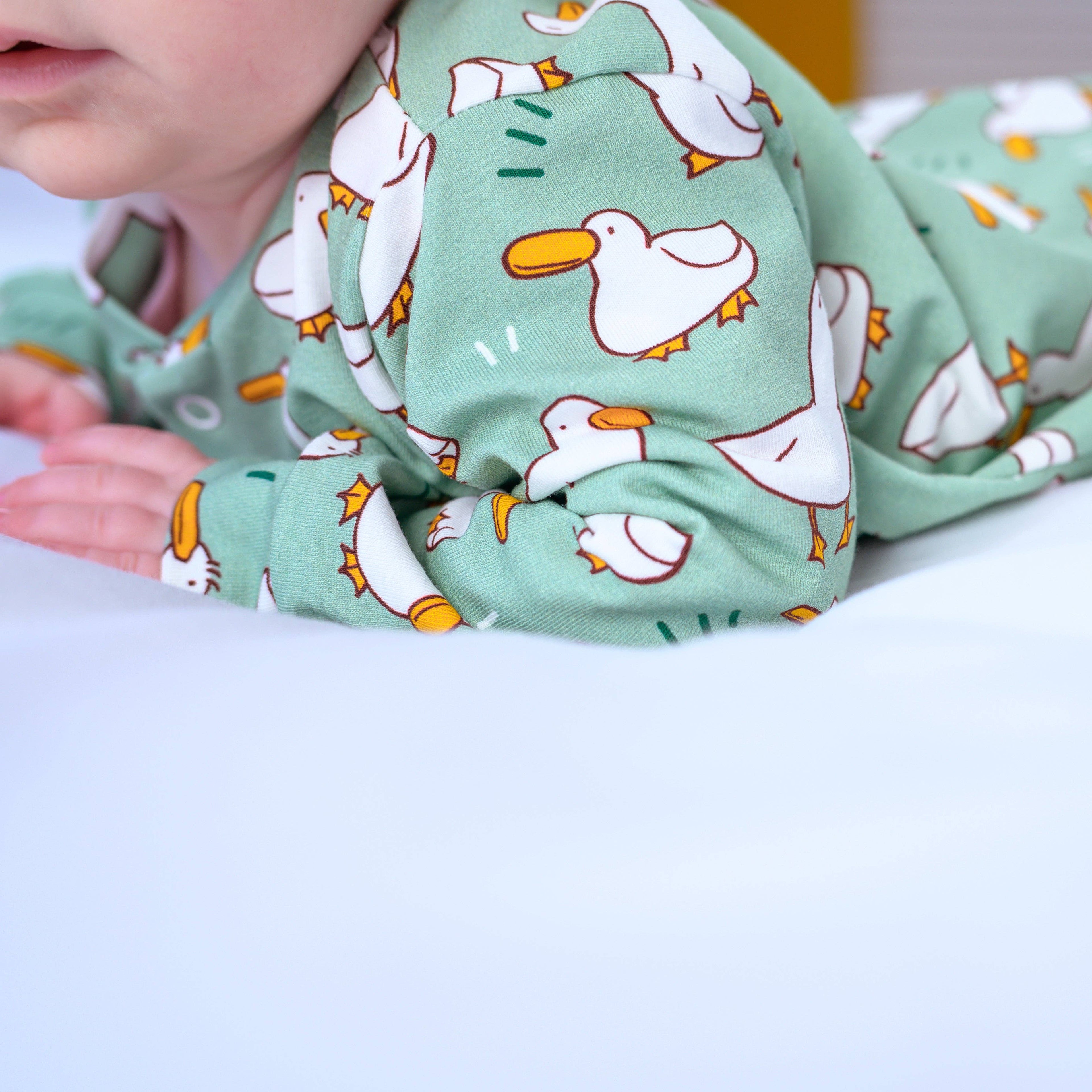 Green sleepsuit with duck pattern worn by a child on a white background