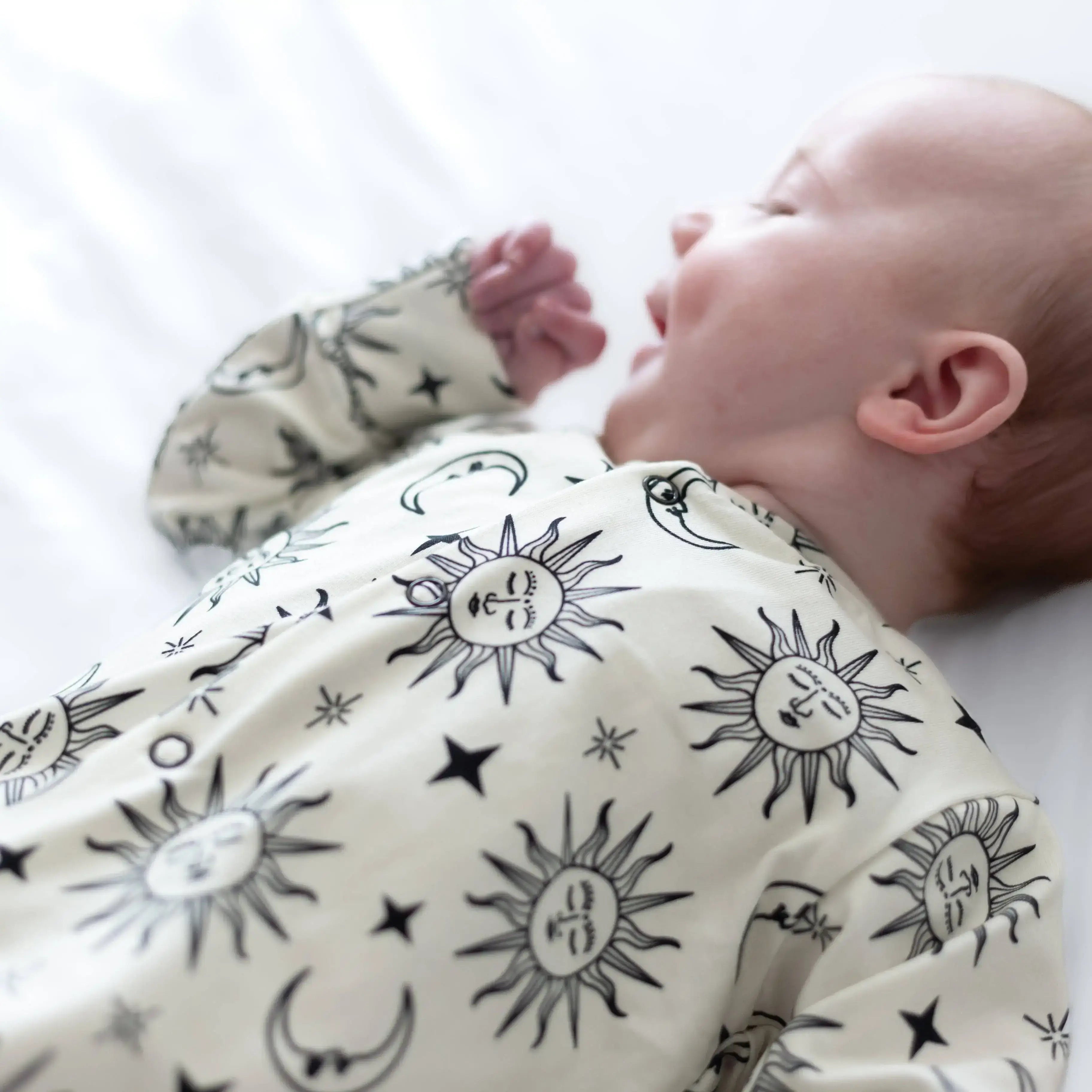 Baby wearing a sleepsuit with celestial patterns on a white background