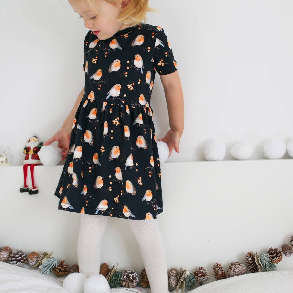 Child wearing a black dress with orange bird pattern in a festive setting.