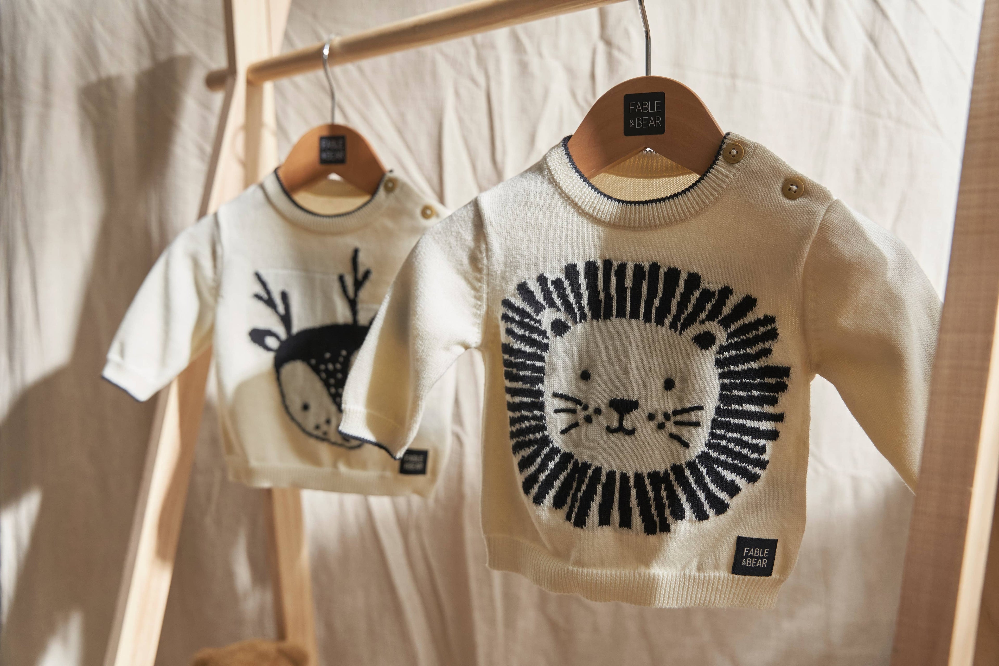 Two children's jumpers/sweaters with animal designs on hangers against a neutral background