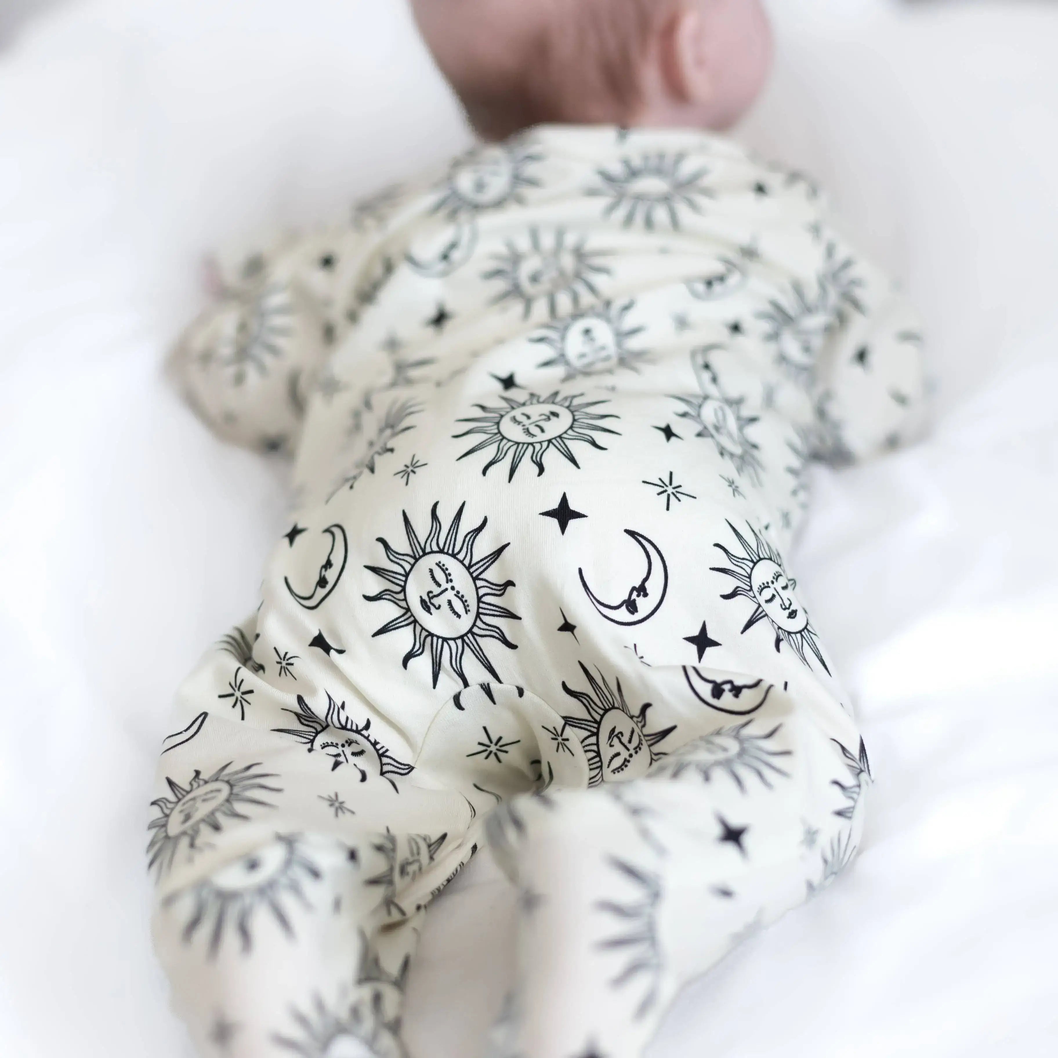 Baby wearing sleepsuit with celestial patterns, held by a hand.