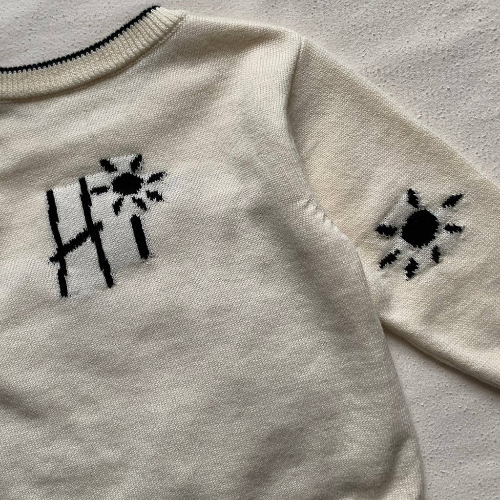 Close-up of a light gray jumper/sweater with black sun designs on sleeves.