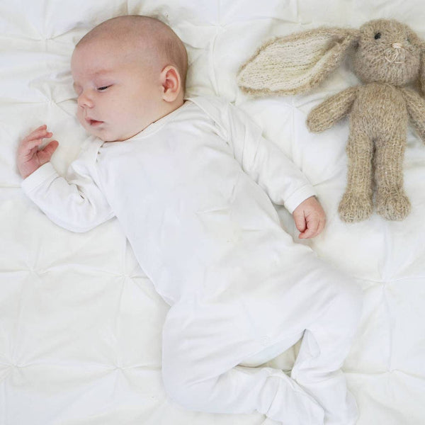 Newborn baby sleeping on a white blanket with a knitted bunny toy next to it