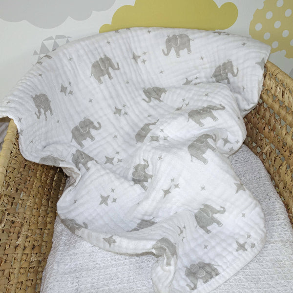 White baby blanket with gray elephant patterns draped over a wicker basket.