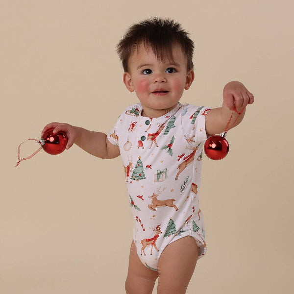 Child wearing a Christmas-themed onesie with red ornaments on a beige background