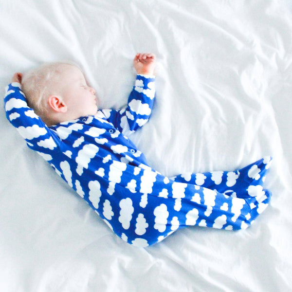 Baby lying on a white blanket wearing a blue and white patterned onesie.