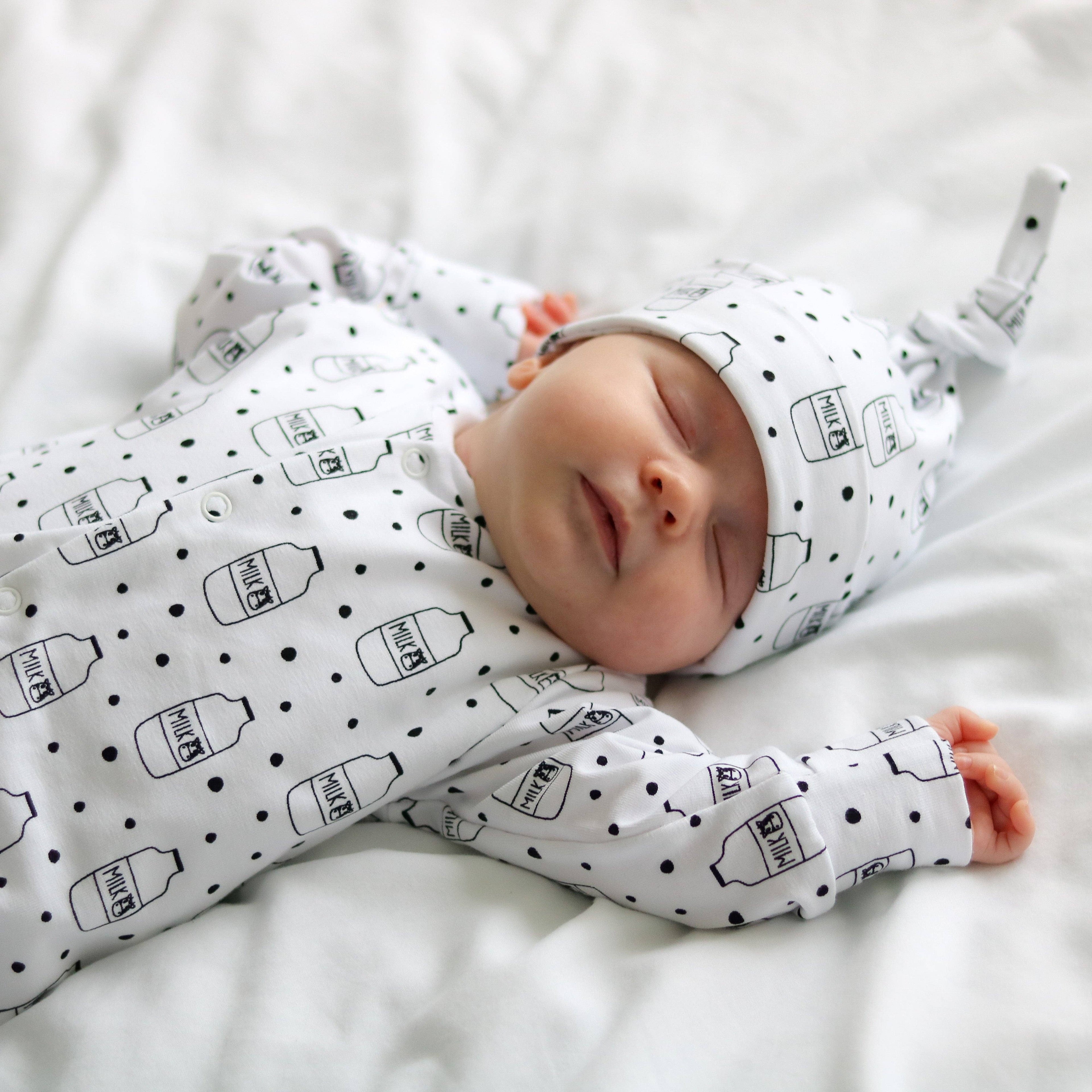 Newborn baby wearing a white sleepsuit with black patterns on a white blanket