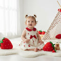 Baby in a red and white dress surrounded by strawberry-themed toys and decorations.